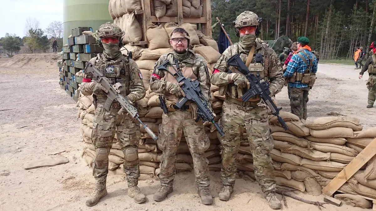 Gruppenbild mit 3 Mitgliedern von Team A.C.E. vor einer Sandsackstellung.